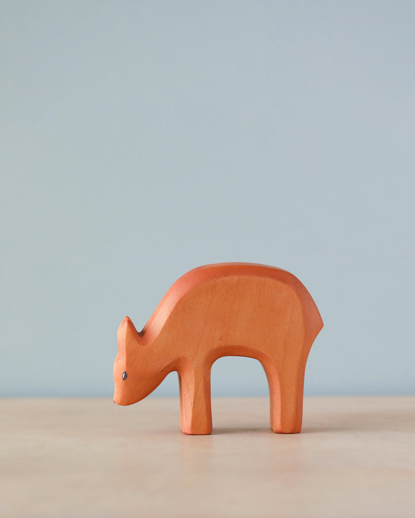 A simple wooden toy bear from the Handmade Holzwald Eating Deer Brand on a plain surface with a pale blue background. The bear is stylized with smooth curves and a natural wood finish.