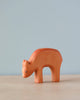 A Handmade Holzwald Eating Deer wooden toy bear on a pale blue background, standing on a smooth surface. The bear is simplistic in design with visible wood grain and a soft orange hue.