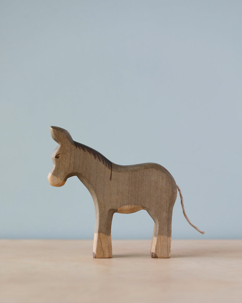 A Handmade Holzwald Donkey, standing side-on, with visible wood grain and texture against a soft blue background. This piece qualifies as an educational toy that showcases natural materials and craftsmanship.