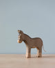 A Handmade Holzwald Donkey stands against a plain light blue background, showcasing a simplistic and smooth design with visible wood grains. This piece is characteristic of sustainable wooden toys.