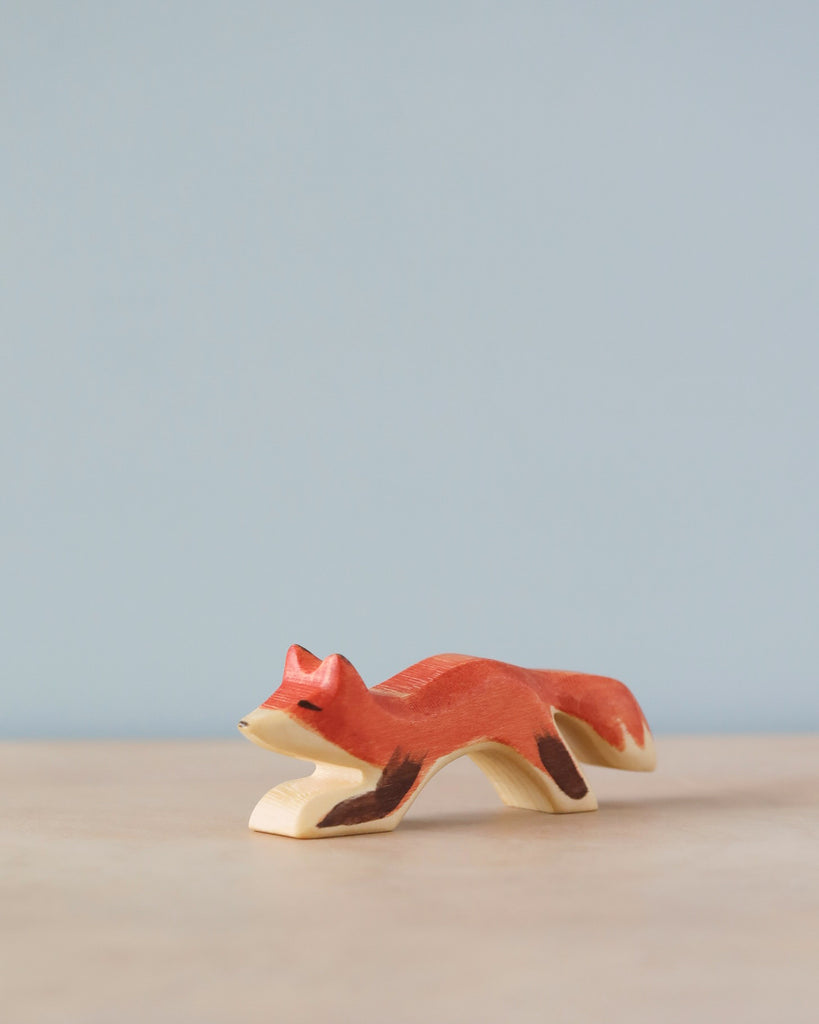 A high-quality Handmade Holzwald Small Fox with a vibrant red body and white details, standing on a light blue surface with a pale blue background.