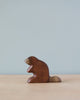 A high-quality Handmade Holzwald Beaver stands on a flat surface against a soft blue background. The figurine is simplistic with smooth contours and a natural wood finish.