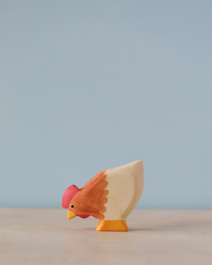 A high-quality Handmade Holzwald Hen painted in natural tones of white, orange, and red, stands against a soft blue background.