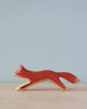 A minimalist Handmade Holzwald Running Fox wooden fox figurine, painted in red with white accents, displayed against a soft blue background.