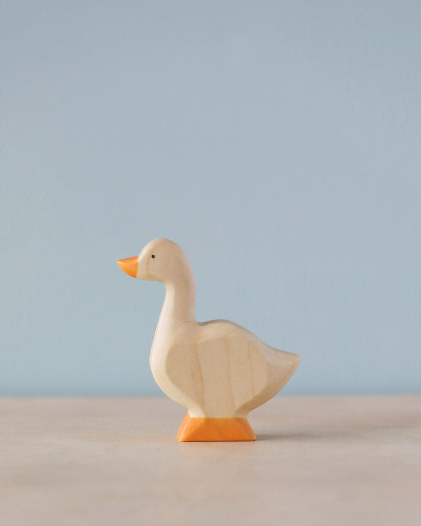 A Handmade Holzwald Goose with a smooth finish, colored with natural dyes, stands against a plain, light blue background.