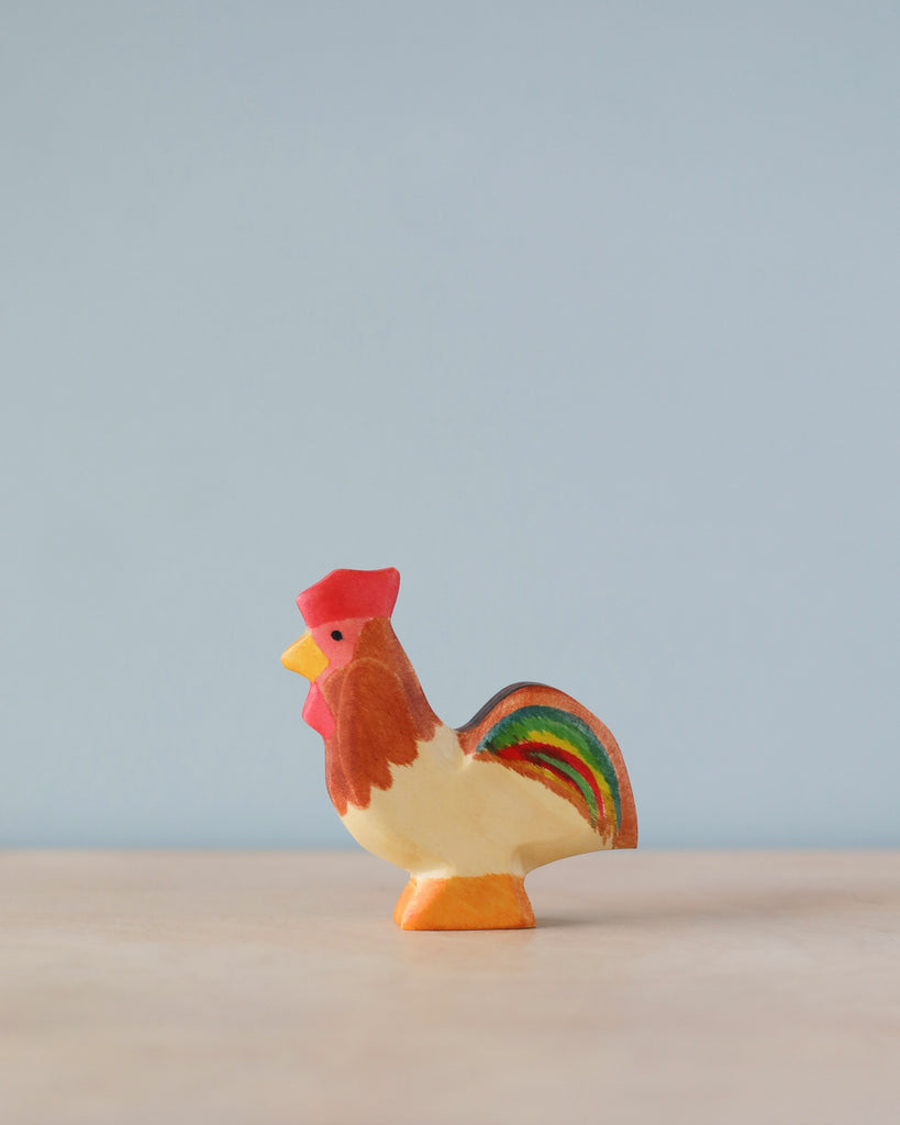 A colorful high-quality Handmade Holzwald Rooster figurine stands against a soft blue background, featuring vibrant red, green, and brown hues on its body.