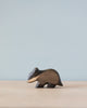 A Handmade Holzwald Badger figurine standing on a plain surface with a soft blue background. This sustainable toy highlights natural wood grains and a smooth finish.