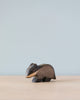 A minimalist image of a small Handmade Holzwald Badger figurine on a plain surface against a soft blue background. The Holzwald Badger, an example of sustainable wooden toys, is carved with smooth curves and dark and light wood.
