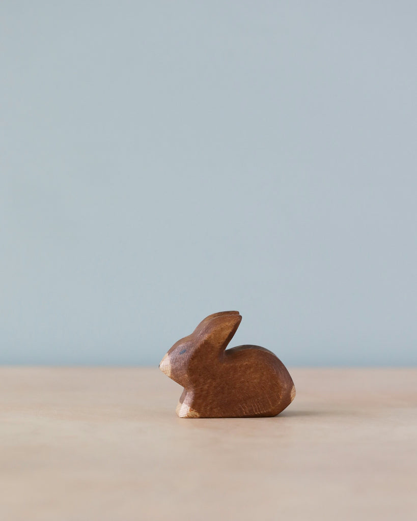 A small, sustainable Handmade Holzwald Small Brown Rabbit figurine on a plain surface with a pale blue background. The figurine is minimalist with smooth, stylized curves.