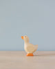 A simple Handmade Holzwald Gosling toy with a high-quality natural finish, featuring an orange beak and feet, stands against a soft blue background.