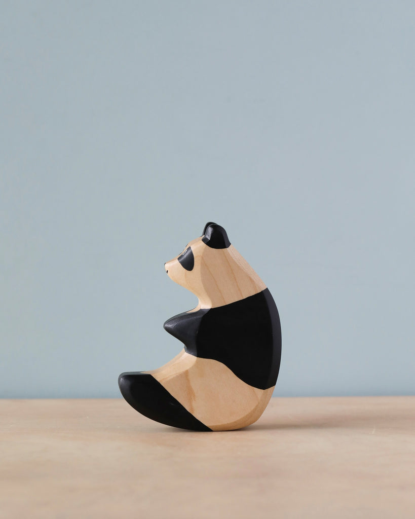 A high-quality Handmade Holzwald Panda toy painted black and white, sitting on a grey surface against a light blue background. The toy is minimalist, emphasizing smooth curves and abstract shapes.