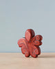 A Handmade Holzwald Octopus, painted in a deep red hue with white dotted details on its tentacles, set against a plain light blue background.