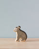 A Handmade Holzwald Koala, painted grey and white, stands against a simple blue-grey background. This sustainable toy is depicted in profile, capturing a poised and lifelike posture.