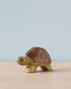 A small Handmade Holzwald Turtle toy with intricate patterns on its shell, standing against a plain blue background with a subtle shadow.