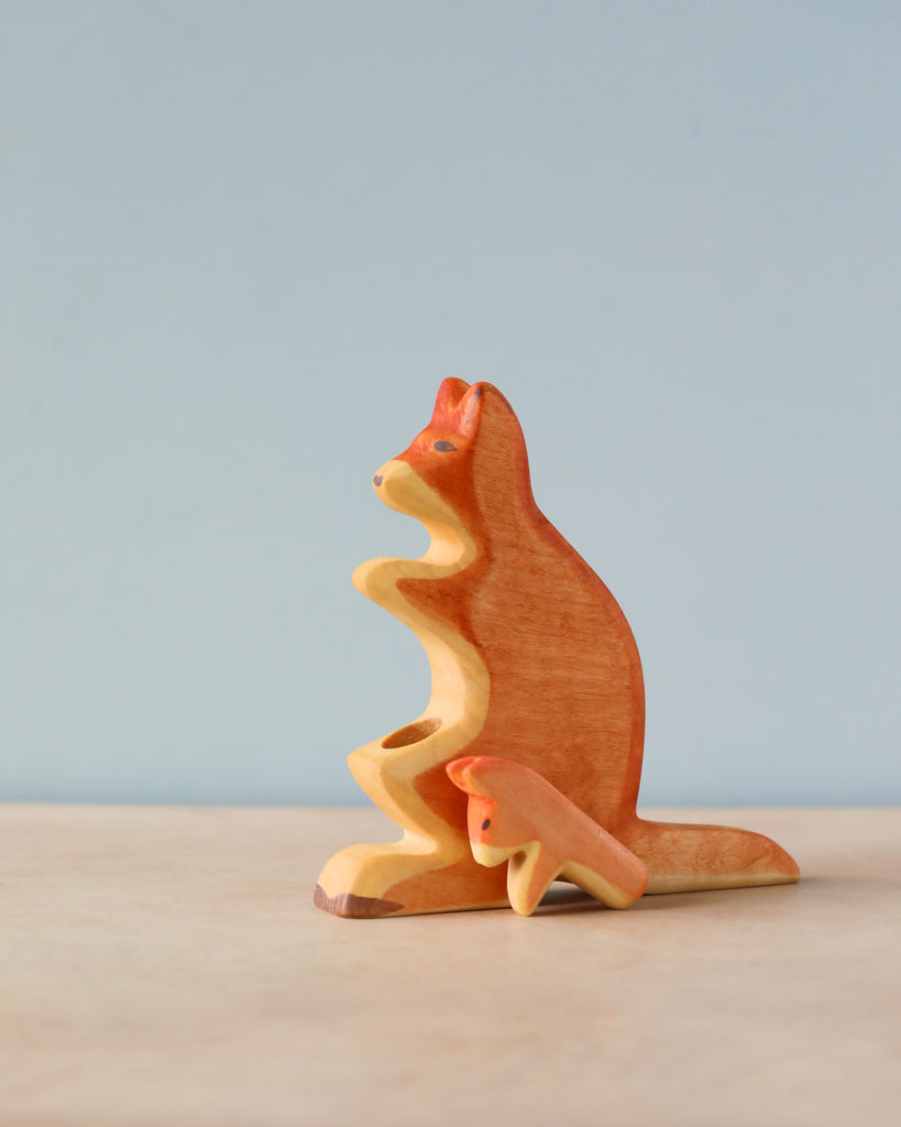 A Handmade Holzwald Kangaroo With Baby sculpture on a plain blue background, showcasing smooth curves and natural wood grain detailing.