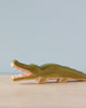 A Handmade Holzwald Crocodile with an open mouth, painted green and cream, positioned on a plain surface against a pale blue background.