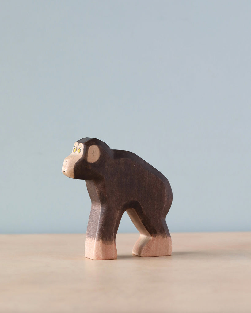 A Handmade Holzwald Chimpanzee figurine, crafted with high-quality dark and light wood finish, stands on a light blue background.