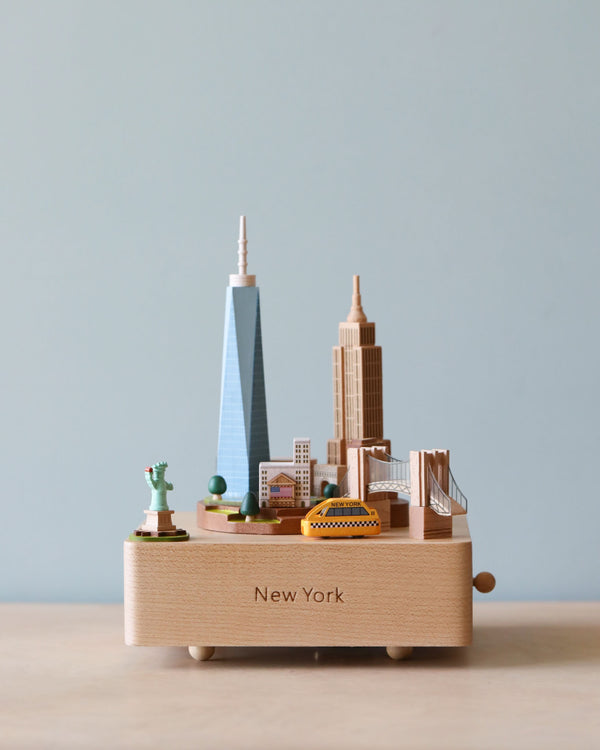 Wooden music box showing a landscape of New York City with Statue of Liberty in the corner and taxi going around. 