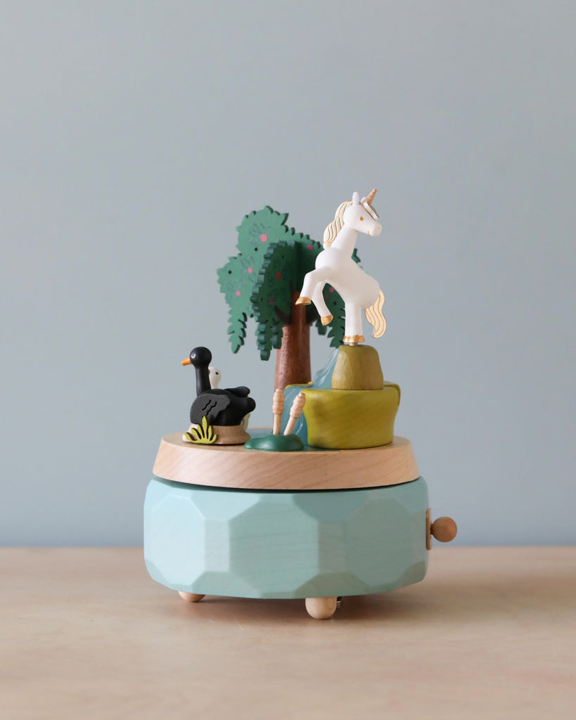 A Unicorn Music Box crafted from sustainably sourced wood, featuring a unicorn, a tree, and an ostrich on a turntable, set against a minimalist grey background.
