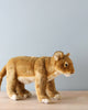 An artisan-crafted Standing Lion Cub Stuffed Animal standing on a wooden surface against a light blue background. The toy is detailed with lifelike colors and features.