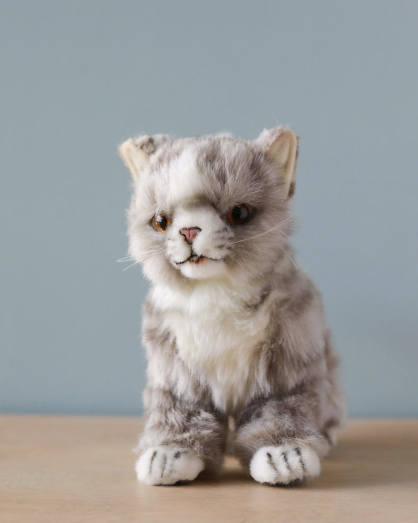 A realistic Grey Cat Stuffed Animal with grey and white fur, sitting upright against a soft blue background. This hand-sewn toy has expressive eyes and detailed facial features.