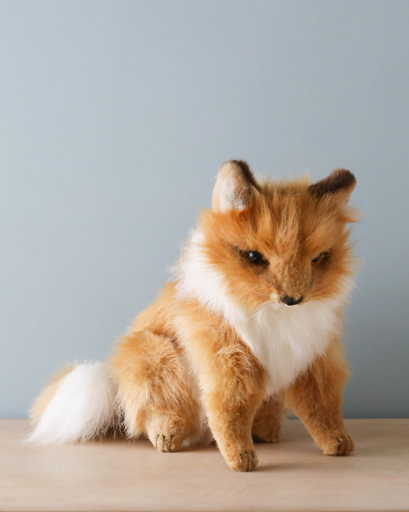 A Sitting Fox Stuffed Animal by HANSA animals, with orange and white fur, sitting against a blue background.
