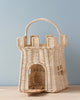 Sentence with product name: Olli Ella | Rattan Castle Bag designed as a magical castle with a handle, featuring a small arched doorway and detailed weaving, set against a plain pale blue background.