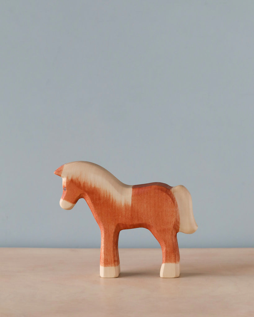 A high-quality Handmade Holzwald Light Brown Horse with a red and white body stands against a light blue background, showcasing simple and smooth craftsmanship.