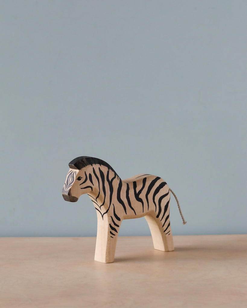 A high-quality Handmade Holzwald Zebra toy with distinct black stripes and a tail, standing against a plain light blue background.