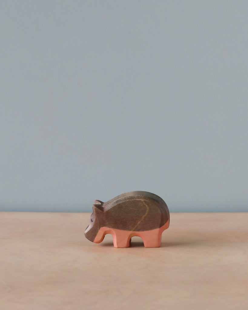 A handmade Holzwald Small Hippo figurine on a plain surface, with a light blue background. The figurine has distinct, segmented body details and pink legs.