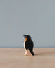 A Handmade Holzwald Penguin figurine, representing sustainable toys, stands against a plain blue-gray background on a light wooden surface, capturing a minimalist aesthetic.