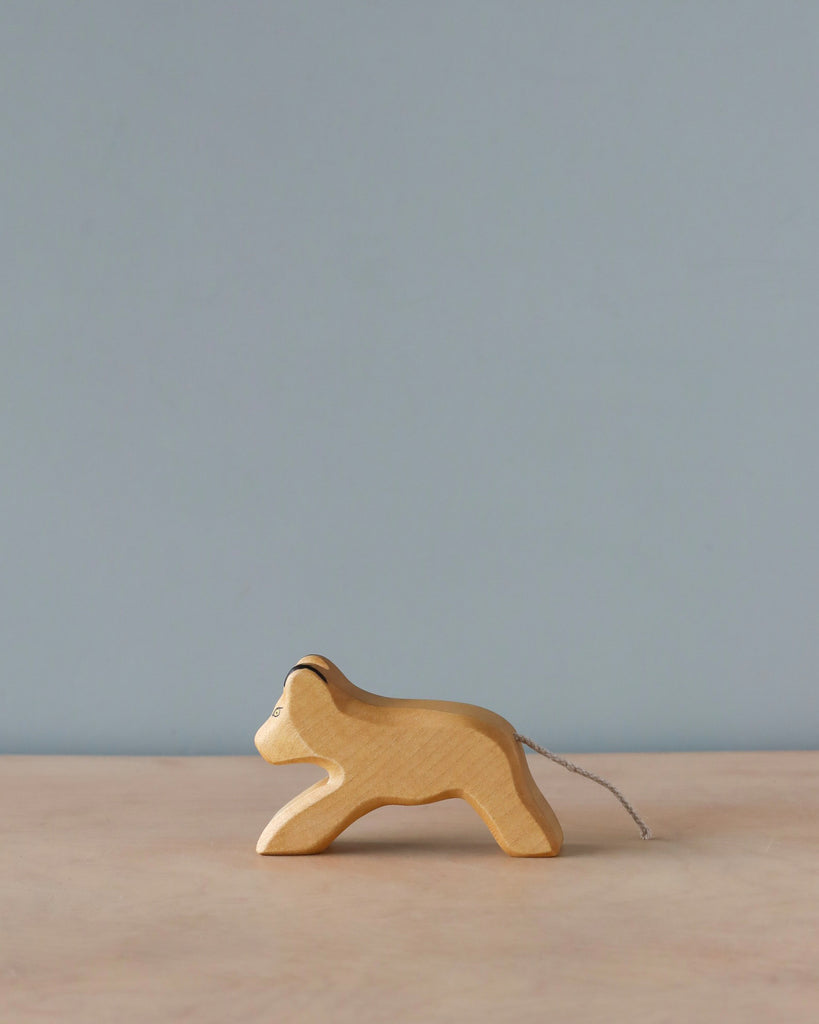 A Handmade Holzwald Lion Cub with a string tail, set against a plain blue background. The lion cub is standing on a light-colored surface, represents sustainable toys crafted from natural materials.