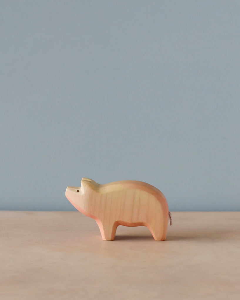A Handmade Holzwald Pig shaped like a piggy bank stands on a plain surface against a light blue background. This sustainable toy features a coin slot on its back.