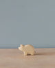 A handmade Holzwald Piglet figurine on a wooden surface against a plain light blue background. The figurine is minimalistic with visible wood grains and represents sustainable toys.