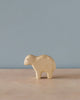 A simple Handmade Holzwald Sheep stands on a plain surface against a light blue background. The toy has minimalist features and is made from sustainable wood, presenting a soft natural finish.
