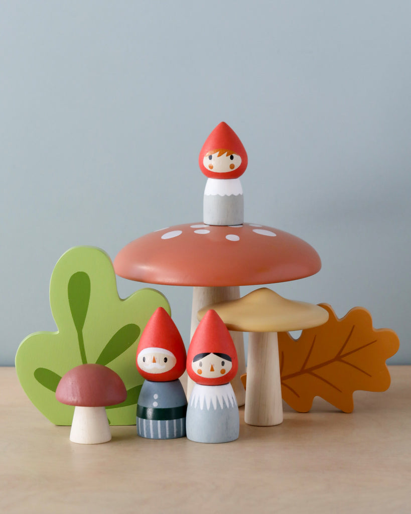 A whimsical display from the Woodland Gnome Family collection featuring three gnome figures and several mushroom and leaf shapes on a light wooden table against a pale blue background.