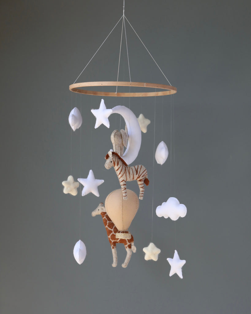 A Handmade Mobile - Day Dreamer - Final Sale featuring a moon, stars, clouds, and plush animals including a giraffe and a zebra, all dangling from a round wooden hoop suspended by strings.