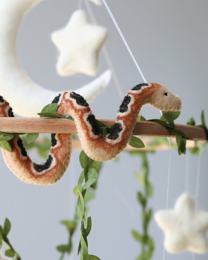 A Handmade Mobile - In The Jungle - Final Sale wrapped around a wooden perch, decorated with artificial leaves, part of a nursery mobile featuring hanging felt stars on a grey background.