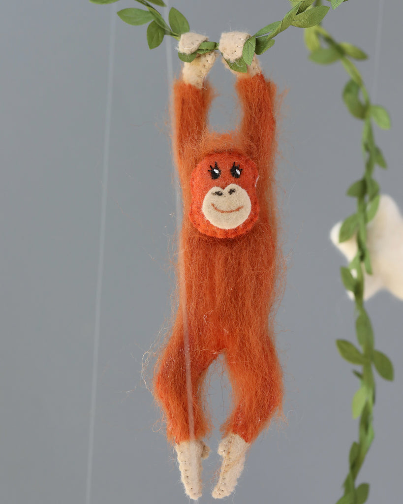 A Handmade Mobile - In The Jungle, designed as a nursery mobile, hangs from a vine, smiling, with a grey background. The orangutan features detailed facial expressions and limbs.