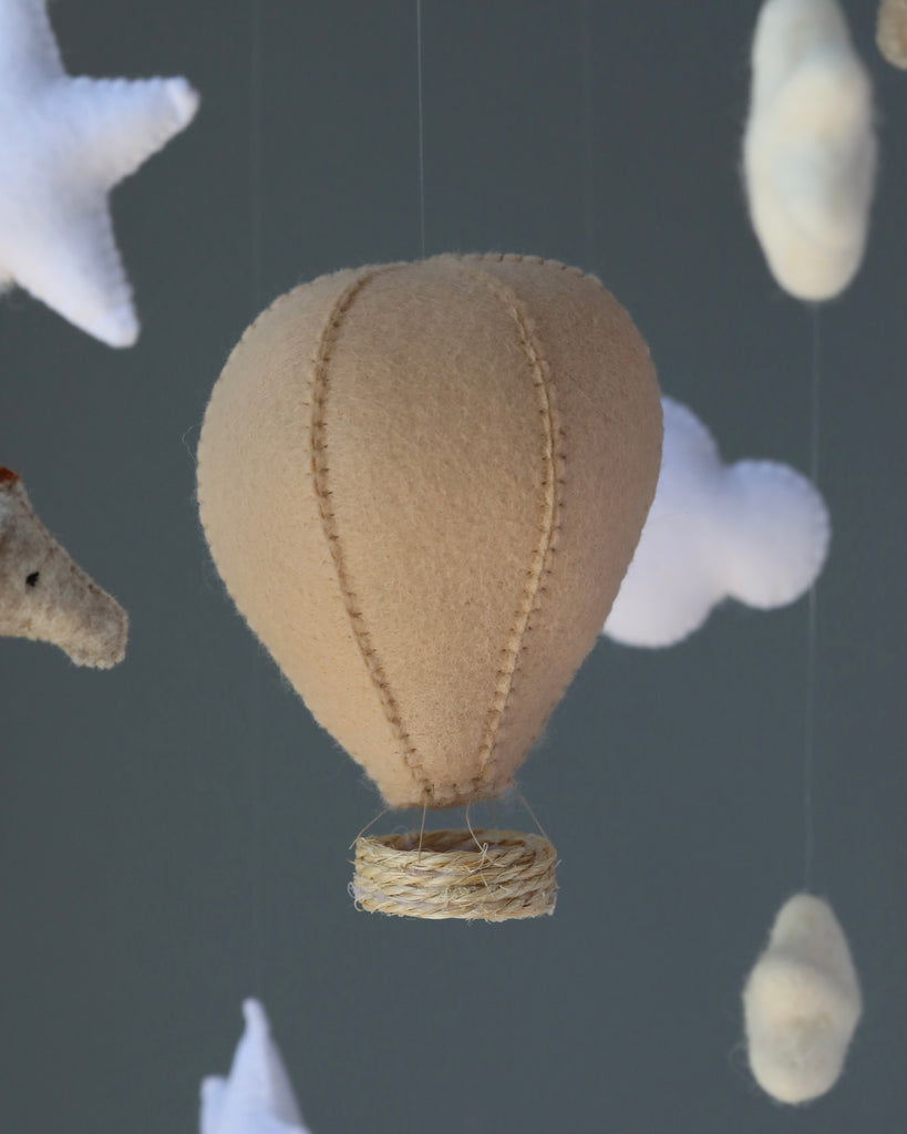 A Day Dreamer handmade mobile and fluffy white clouds are artistically arranged as a nursery mobile, set against a soft gray background. The balloon is suspended by thin strings, suggesting gentle motion.