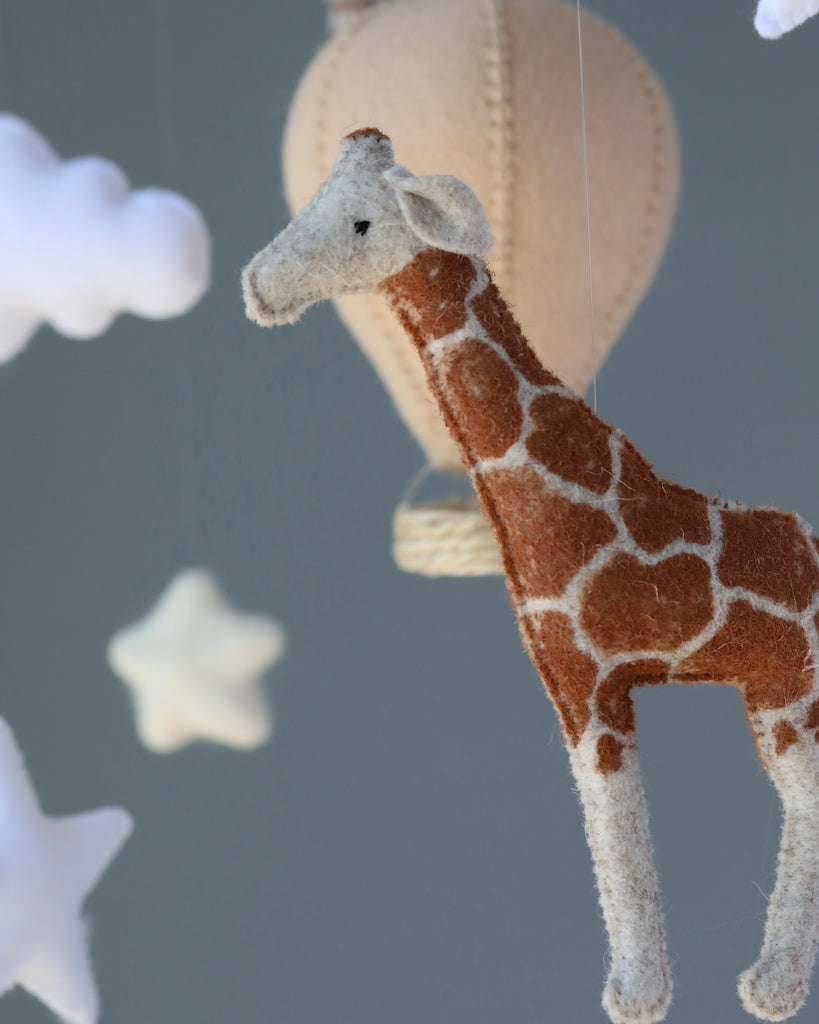 A close-up of a Handmade Mobile - Day Dreamer - Final Sale in a nursery ceiling mobile, surrounded by felt clouds and stars, highlighted against a soft gray background.