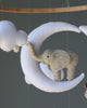 A Handmade Mobile - Day Dreamer - Final Sale elephant toy standing on a white crescent moon, both components of the mobile, hanging from strings against a blurred background.