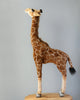 A Medium Giraffe Stuffed Animal, 34'', meticulously hand-sewn, stands upright against a plain gray background, displaying distinct brown patches on its body and a long neck. Its eyes are large and expressive.