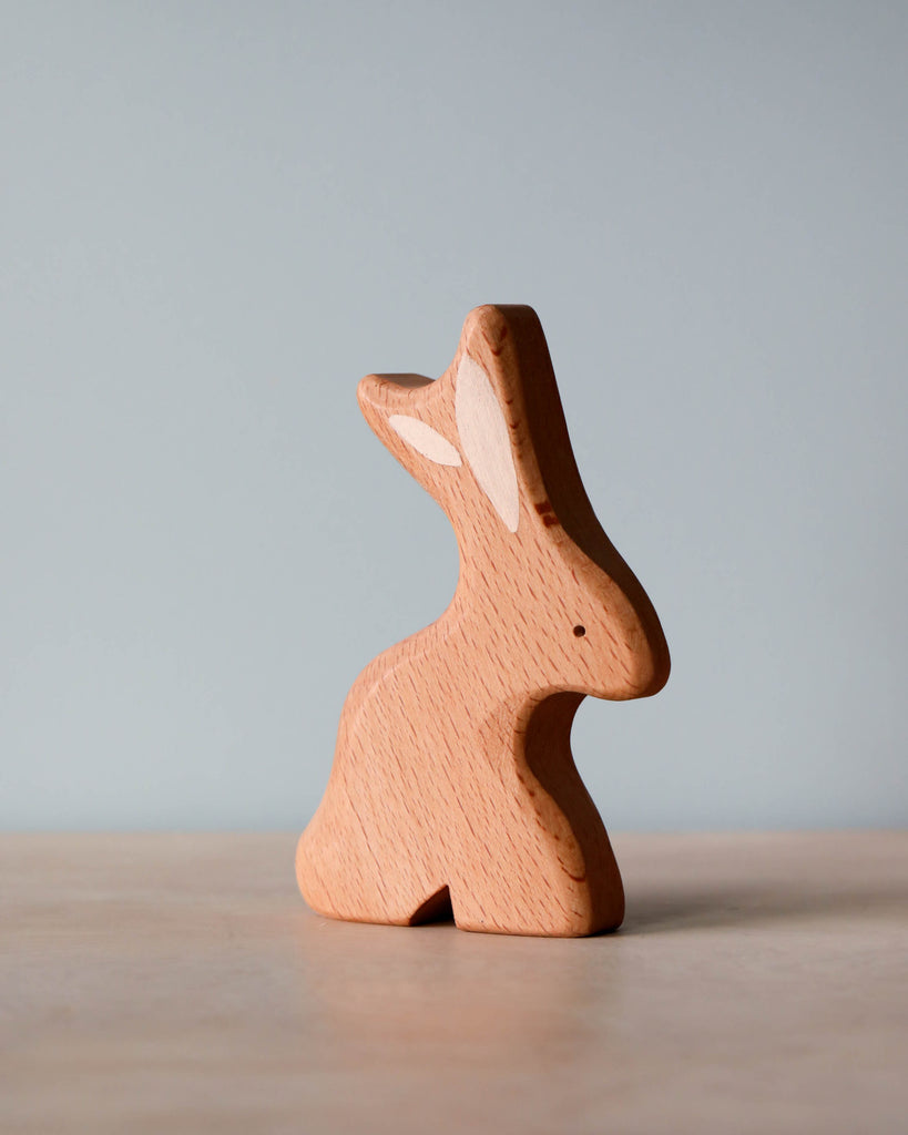 A simple Handmade Wooden Bunny from Tevi Toys stands against a soft blue background, showcasing smooth edges and a minimalist design.