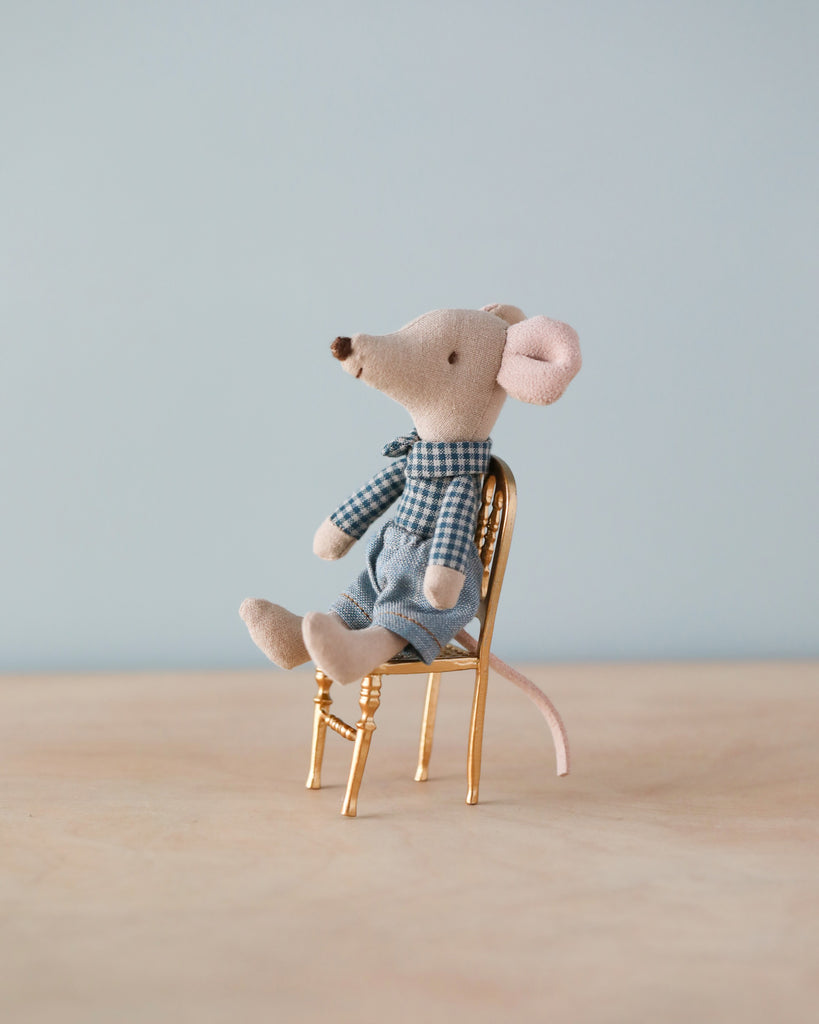 Beige cloth mouse with blue plants and lea and white checkered shirt sitting on gold metal chair. Natural color counter and light blue background. 