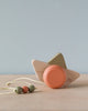 A minimalist wooden toy pull-along, the Handmade Wooden Boat Pull Toy, handmade in Ukraine, in the shape of a duck with a coral-colored sphere for a body and light wood wings, set against a pale blue background.