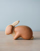 A Handmade Wooden Bunny with smooth, curved lines and visible wood grain, crafted from sustainably harvested hardwood, displayed on a plain surface against a soft blue background.