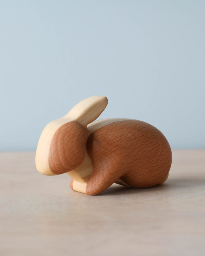 A Handmade Wooden Bunny figurine, crafted from sustainably harvested hardwood with different grains, placed on a surface against a soft blue background.