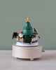 The Santa & Reindeer Music Box, a hand-cranked wooden piece, displays a festive scene featuring Santa with gifts, a reindeer, and a Christmas tree topped with a star. Designed solely for decorative use, it is crafted from sustainably sourced wood set against a gentle green backdrop.