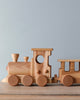A handmade Handmade Wooden Train - Extra Long set consisting of an engine and two cars, featuring smooth, natural beech wood tones against a soft blue background.